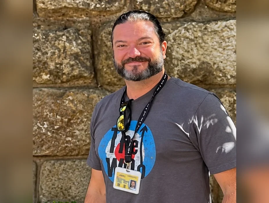 Samuel, official tourist guide in Seville, wearing his guide license badge in front of an old stone wall